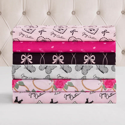 Five folded, patterned fabrics in pink, black, gray, and white—featuring bows, hearts, roses, teddy bears, and Juicy Couture text—showcase the Microfiber Sheet Set With Extra Pillowcases to elevate your luxury bedding against a tufted headboard.