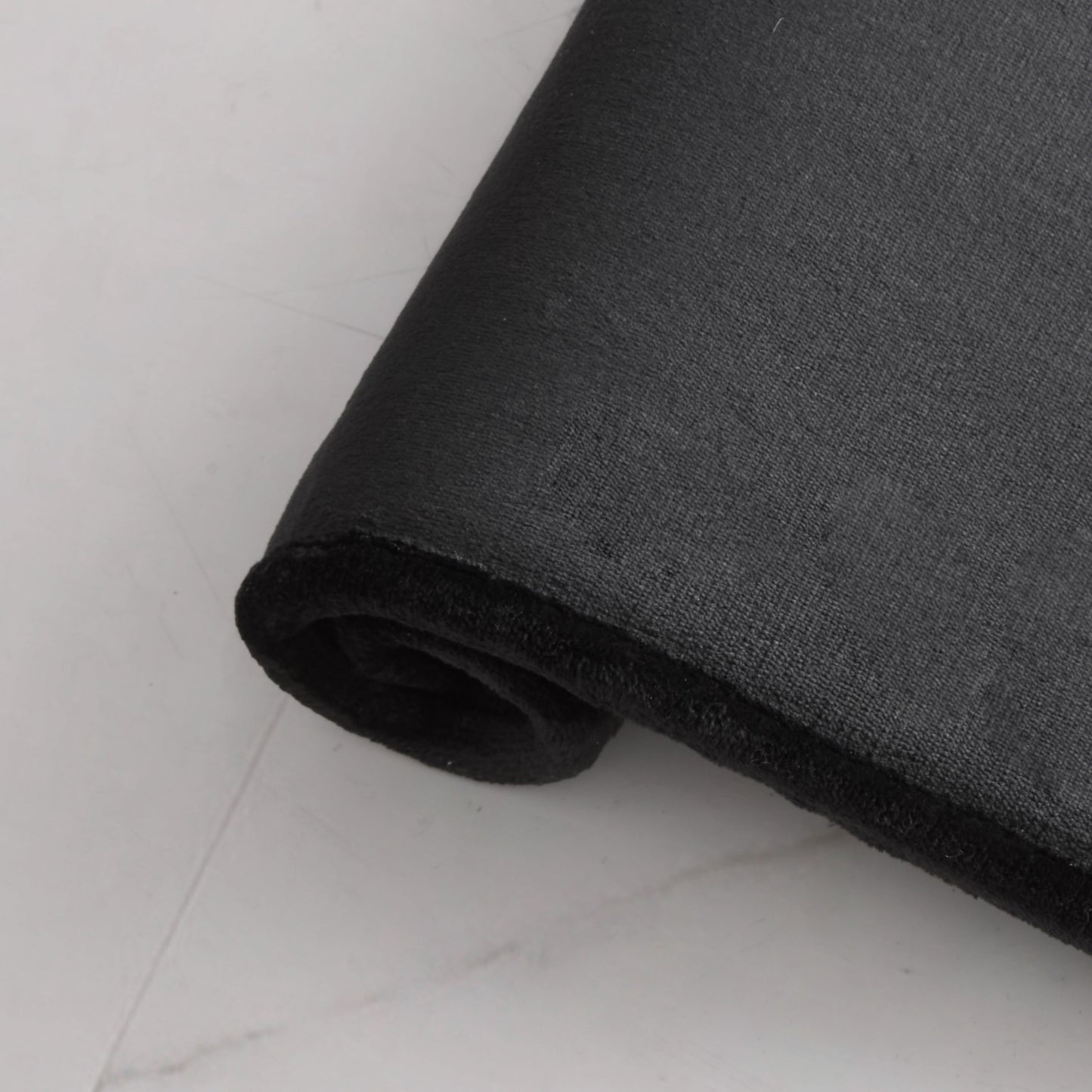 A close-up of the Quilted Memory Foam Bath Mat, 17" x 24", in black, resting on a white surface highlights its textured and thick design that offers a luxurious feel.