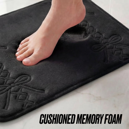A bare foot steps onto the Quilted Memory Foam Bath Mat, 17" x 24", with decorative patterns, on a light floor. The text CUSHIONED MEMORY FOAM appears at the bottom.