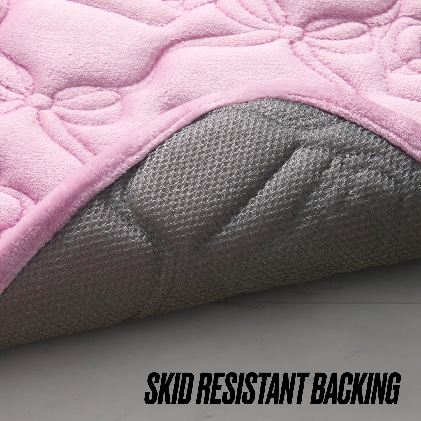 A close-up of a pink Quilted Memory Foam Bath Mat, 17" x 24", with the corner lifted to reveal its gray, skid-resistant backing. "SKID RESISTANT BACKING" is displayed at the bottom of the image.