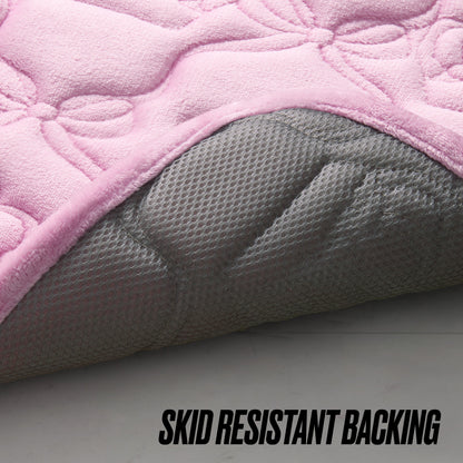 A close-up of a pink Quilted Memory Foam Bath Mat, 17" x 24", with the corner lifted to reveal its gray, skid-resistant backing. "SKID RESISTANT BACKING" is displayed at the bottom of the image.