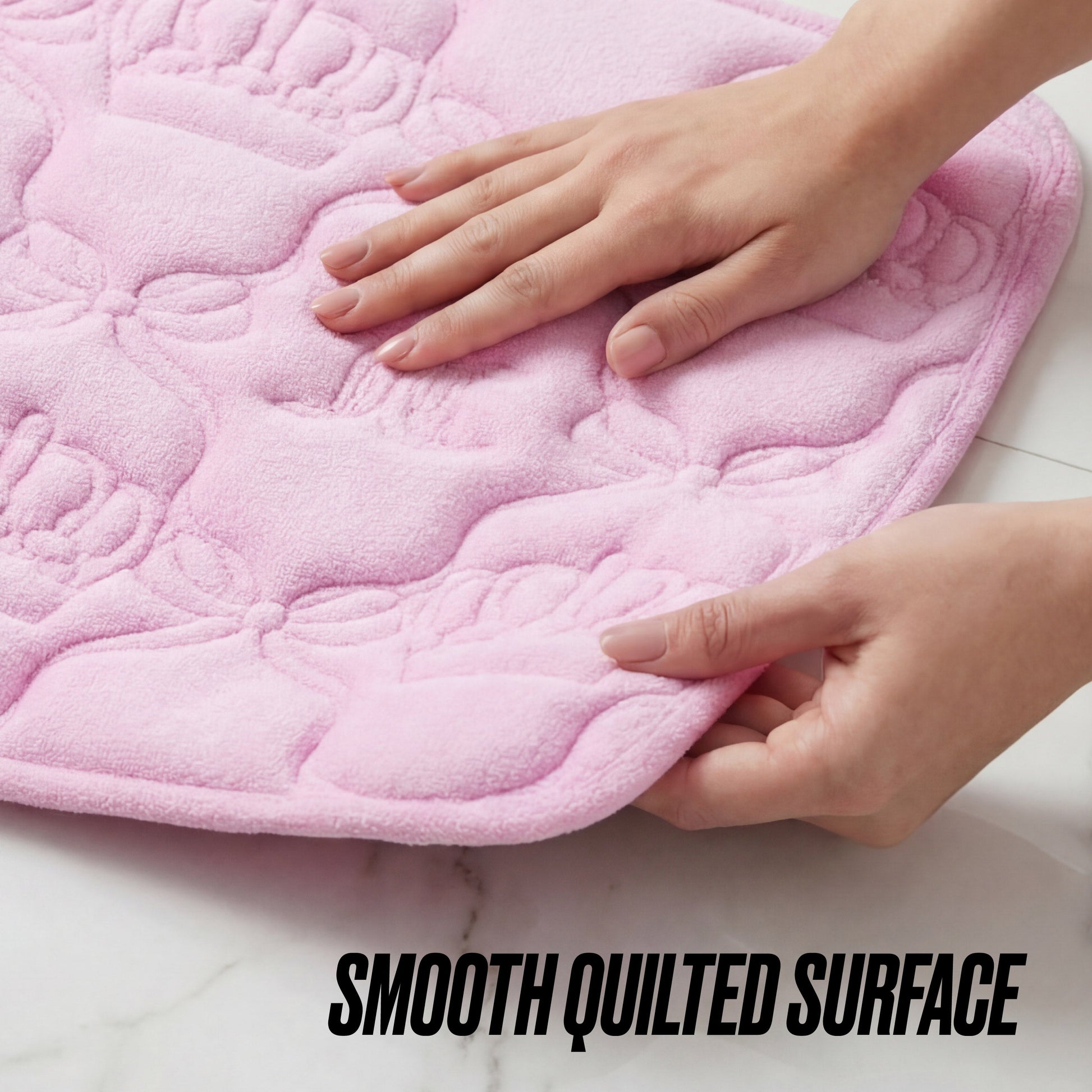 A hand lifts the edge of a soft, pink Quilted Memory Foam Bath Mat, 17" x 24", featuring a crown pattern; “SMOOTH QUILTED SURFACE” appears at the bottom right.