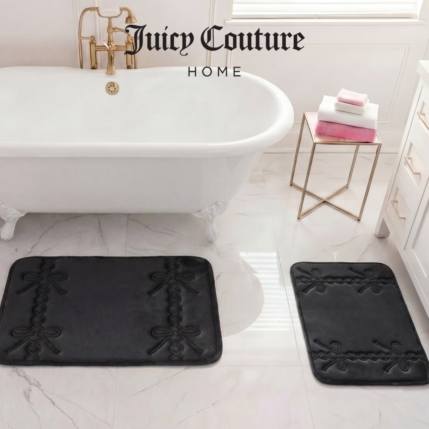 A white bathroom with a clawfoot tub, gold fixtures, a luxury Juicy Couture Quilted Memory Foam Bath Mat 2-Piece Set in black and white, a side table with folded pink and white towels, and "Juicy Couture HOME" at the top.