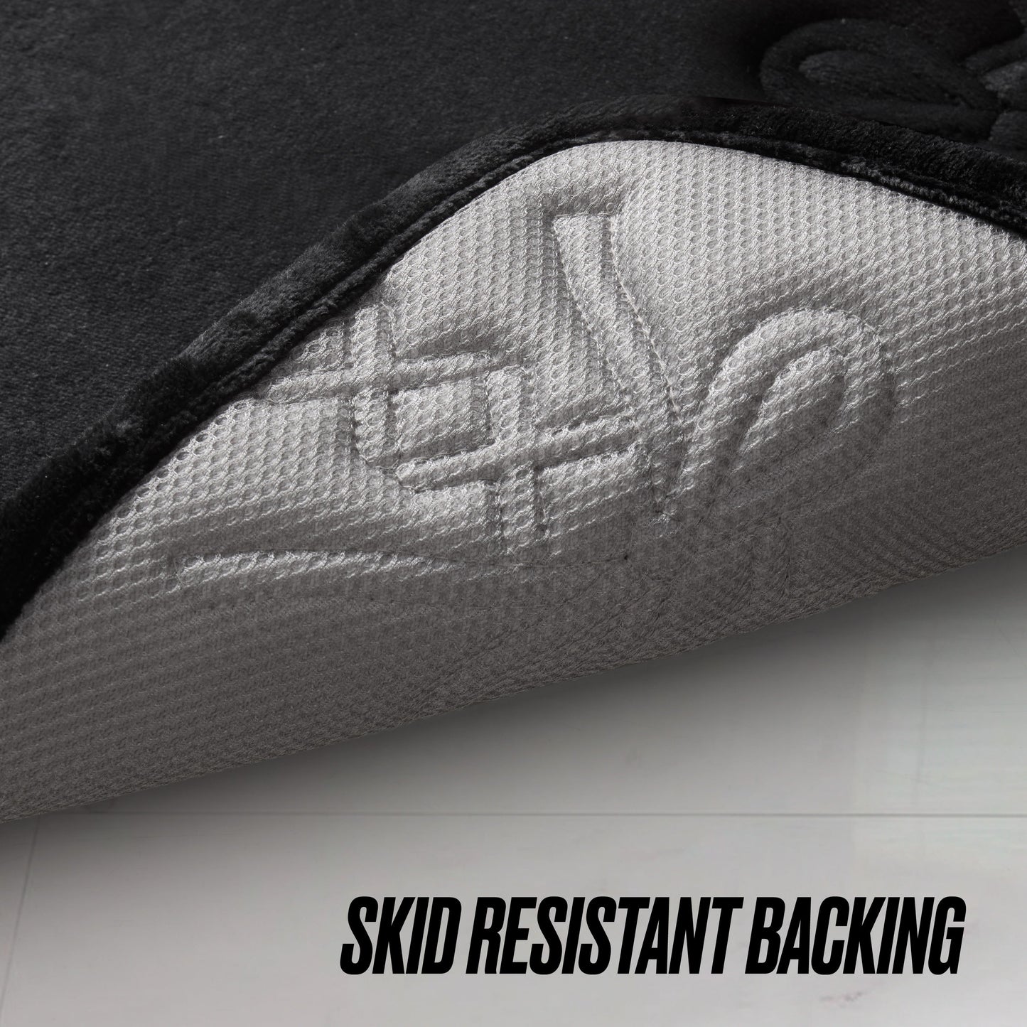 A close-up shows the corner of the Quilted Memory Foam Bath Mat 2-Piece Set lifted to reveal its textured, light gray backing. “SKID RESISTANT BACKING” is displayed below, emphasizing this set’s secure and safe design.
