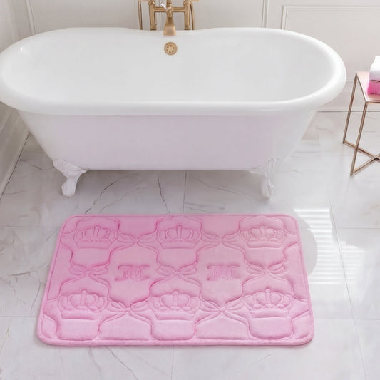 A white clawfoot bathtub sits in a marble-tiled bathroom with a plush Quilted Memory Foam Bath Mat (20" x 32") placed in front. A small gold side table nearby holds a white and pink bottle.