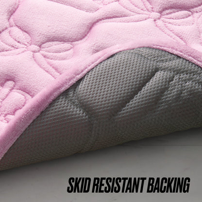 A close-up of the Quilted Memory Foam Bath Mat, 20" x 32", in pink, with the corner lifted to show its textured gray skid-resistant backing. The words SKID RESISTANT BACKING appear at the bottom right.