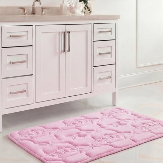 A Quilted Memory Foam Bath Mat, 20" x 32", in light pink with a floral pattern is placed on a glossy white tile floor in front of a white bathroom vanity with silver handles.
