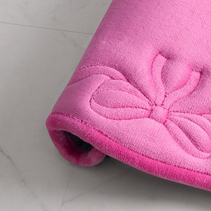 A close-up of a soft, rolled-up Quilted Memory Foam Bath Mat, 17" x 24", featuring a textured butterfly pattern on the surface, placed on a light-colored floor.