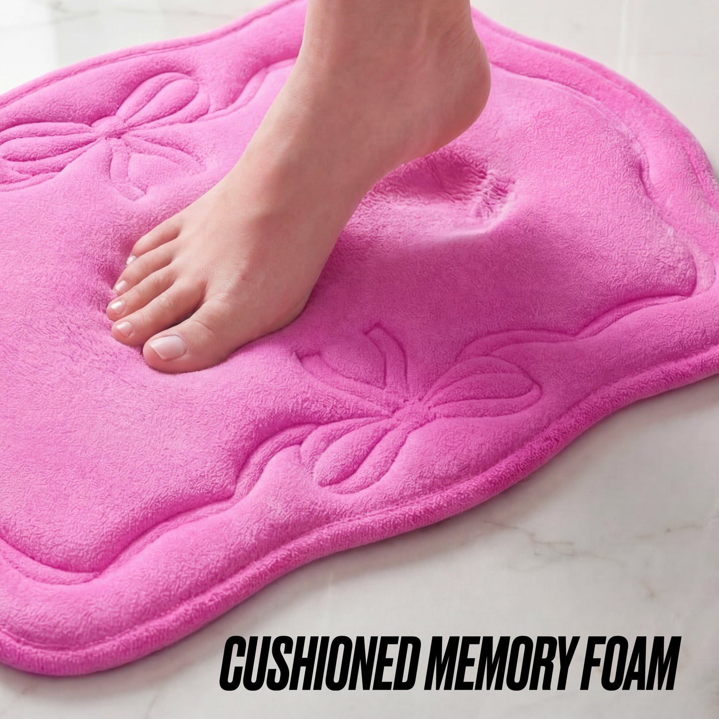 A bare foot steps onto the pink Quilted Memory Foam Bath Mat, 17" x 24", with decorative bows, leaving an indentation. "CUSHIONED MEMORY FOAM" is printed at the bottom.