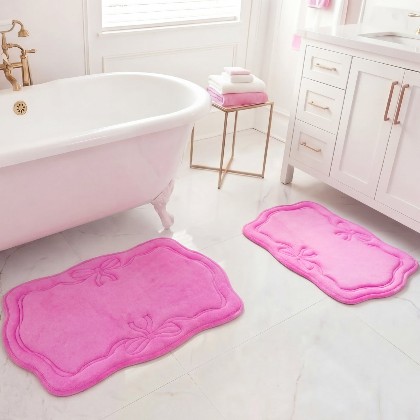 The bright, clean bathroom features the Quilted Memory Foam Bath Mat 2-Piece Set in pink on a white marble floor near a clawfoot tub and vanity, with towels stacked on a gold table by the window.