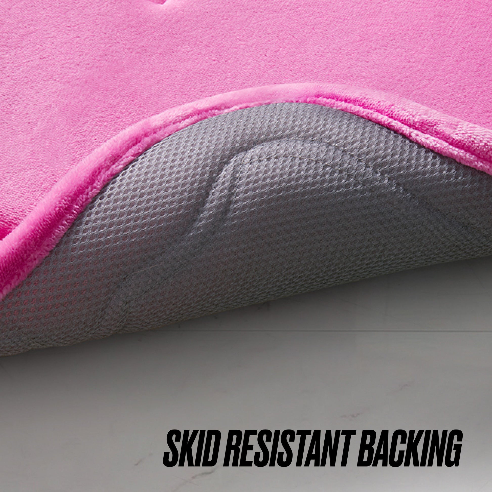 Close-up of the Quilted Memory Foam Bath Mat 2-Piece Set in pink, showing its corner lifted to reveal a textured gray, anti-slip backing. "SKID RESISTANT BACKING" is printed at the bottom of the image.