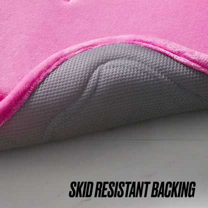 Close-up of the Quilted Memory Foam Bath Mat 2-Piece Set in pink, showing its corner lifted to reveal a textured gray, anti-slip backing. "SKID RESISTANT BACKING" is printed at the bottom of the image.