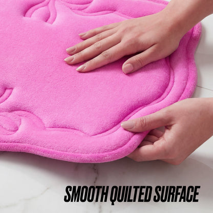 Two hands touch the soft, quilted surface of a pink Quilted Memory Foam Bath Mat 2-Piece Set with wavy edges, shown on a white background. Text below reads: SMOOTH QUILTED SURFACE.