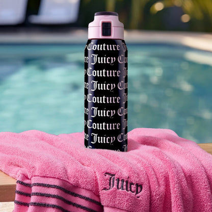A black Glam Getaway Hydration Stainless Steel Tumbler with white Juicy Couture logos sits on a pink Juicy towel by the pool, surrounded by sparkling water and poolside chairs.