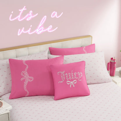 A neatly made Hotel Stripe Leopard Bows Bed in a Bag Bedding Set in pink and white, with “Juicy” pillows featuring bow designs. A neon sign reading “its a vibe” glows on the pale pink wall above the bed.