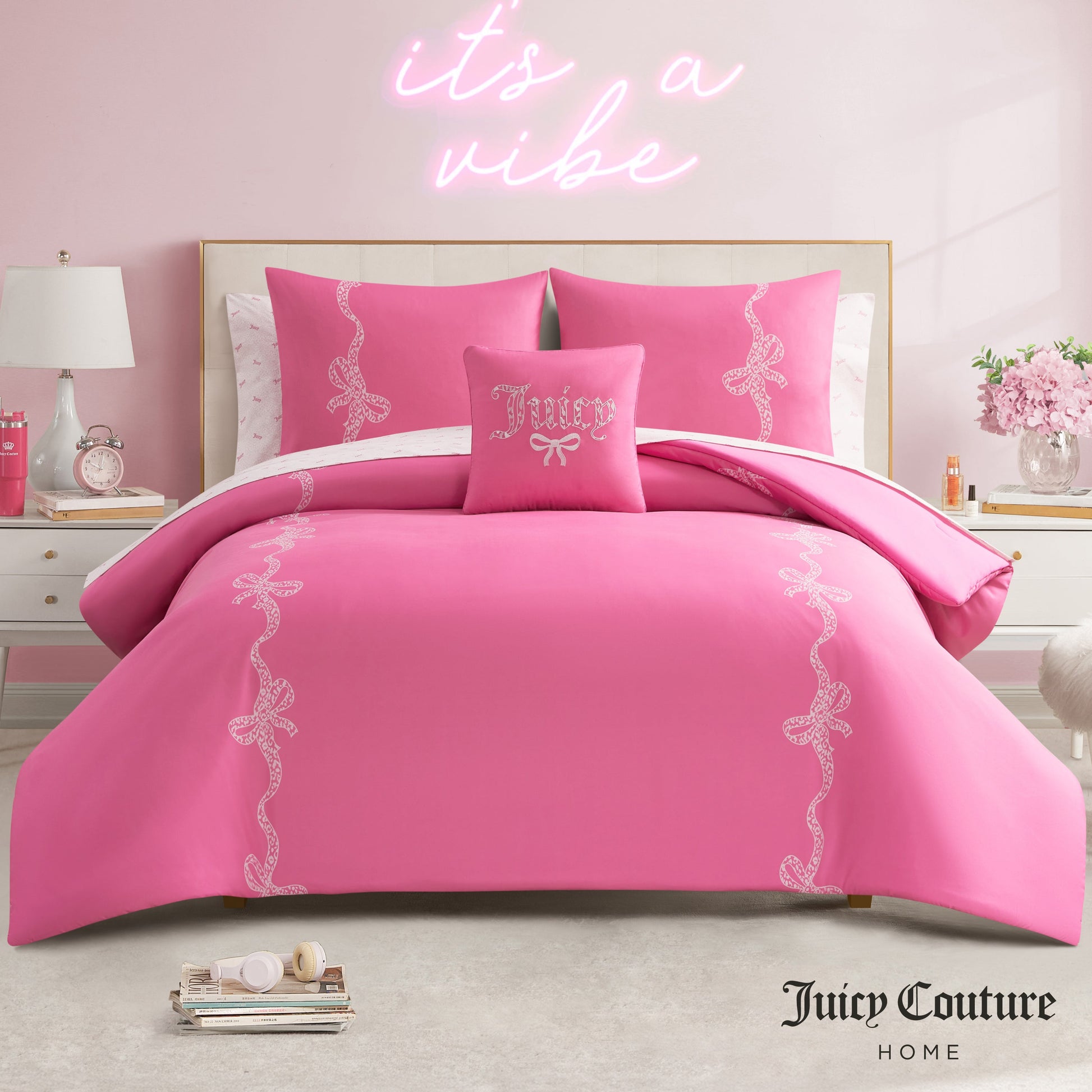 A bedroom with a pink Hotel Stripe Leopard Bows Bed in a Bag Bedding Set, decorative bows, a pink neon "it's a vibe" sign above the bed, light pink walls, white furniture, and various decorative accents.