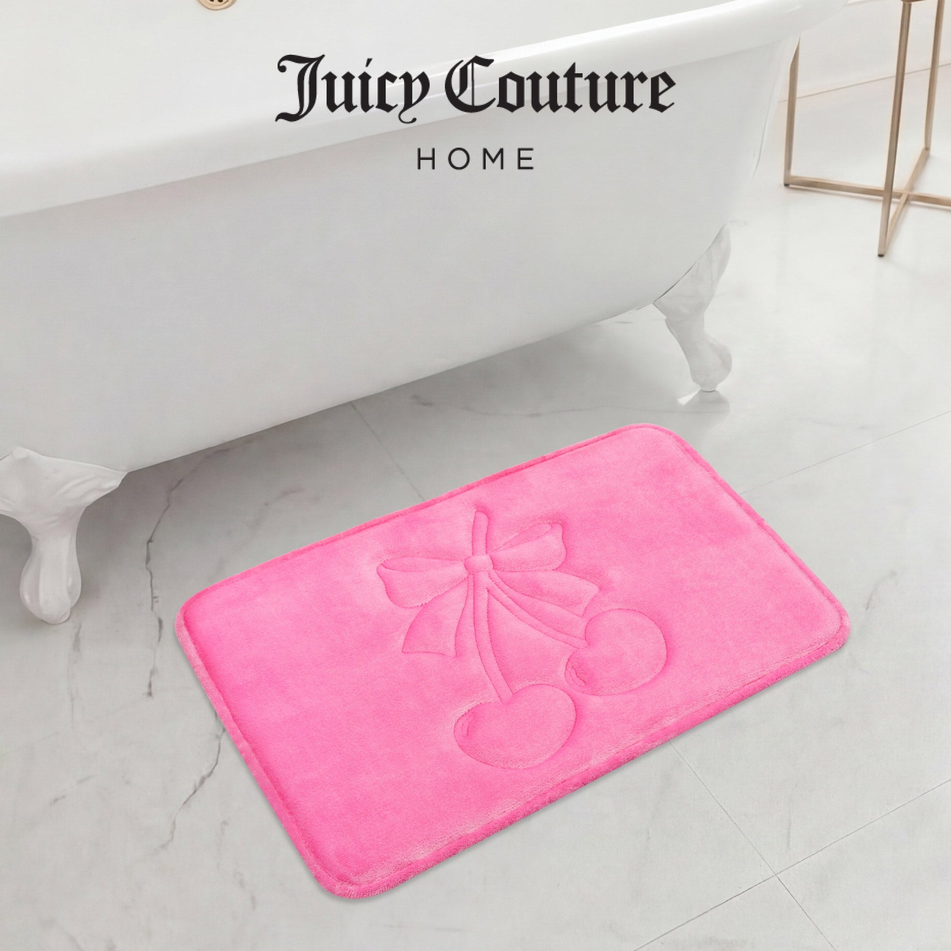 A bright pink Quilted Memory Foam Bath Mat, 17" x 24", with an embossed cherry and bow design sits on a white marble floor in front of a clawfoot tub, adding a stylish touch to your bathroom.