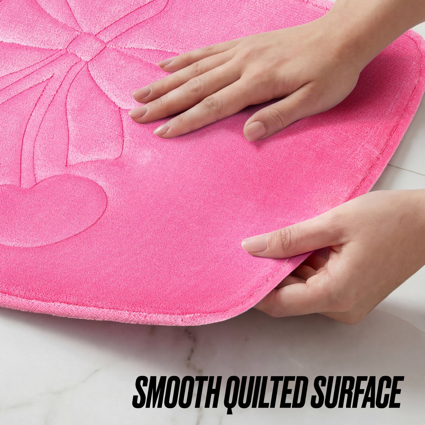 Hands lift the corner of a bright pink Quilted Memory Foam Bath Mat, 17" x 24", showing its smooth, soft quilted surface. The phrase SMOOTH QUILTED SURFACE is displayed at the bottom.