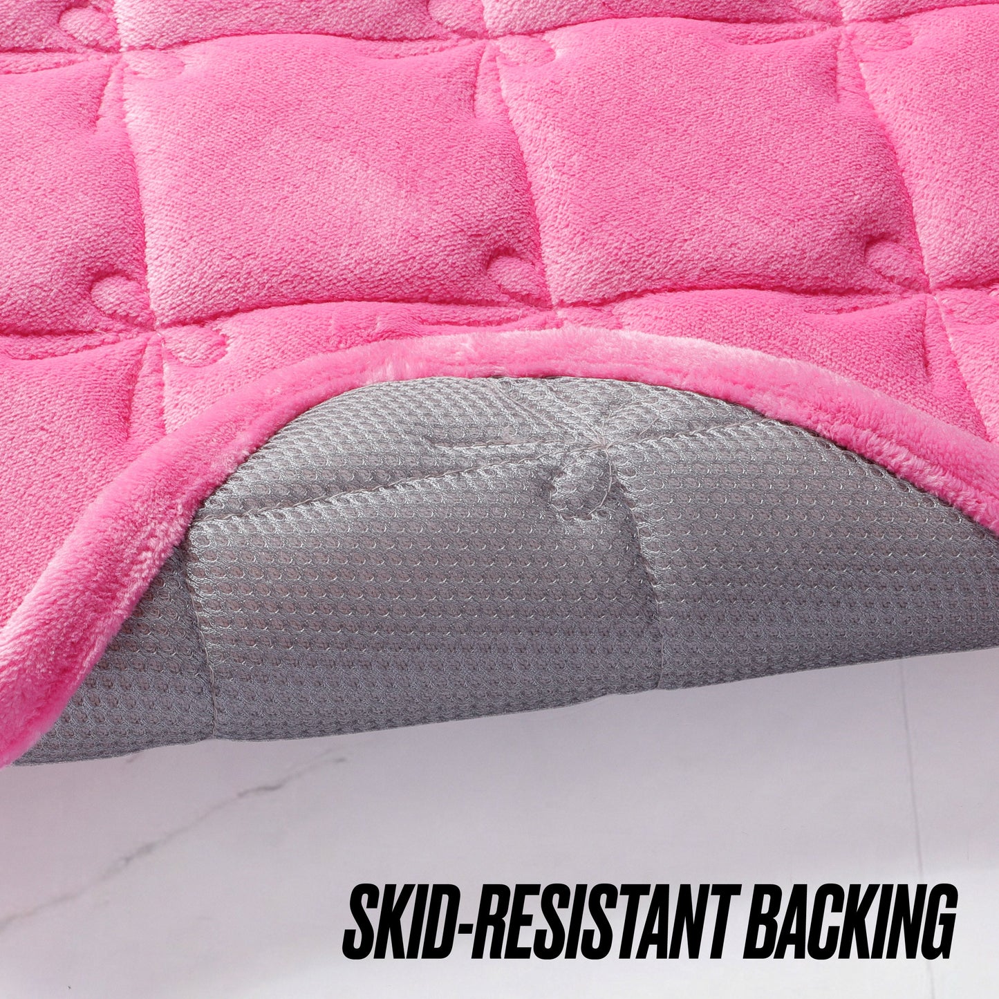 Close-up of a pink Quilted Memory Foam Bath Mat 2-Piece Set by Juicy Couture with the corner flipped up to show the gray, textured, skid-resistant backing. SKID-RESISTANT BACKING is boldly printed at the bottom.