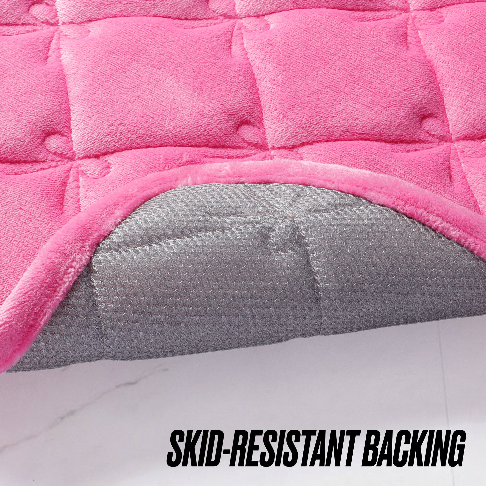 Close-up of a pink Quilted Memory Foam Bath Mat 2-Piece Set by Juicy Couture with the corner flipped up to show the gray, textured, skid-resistant backing. SKID-RESISTANT BACKING is boldly printed at the bottom.