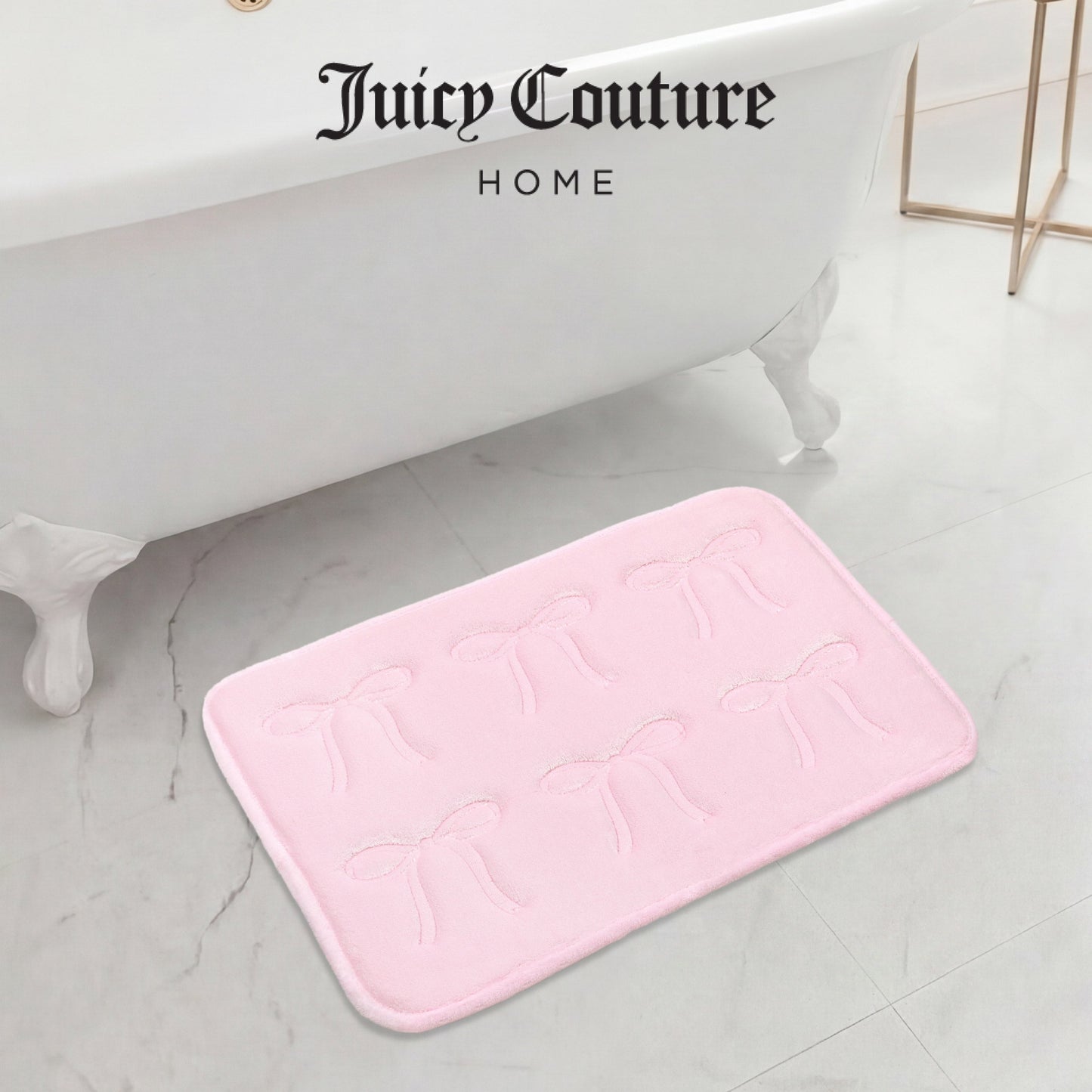 A pale pink Juicy Couture Quilted Memory Foam Bath Mat, 17" x 24", with embossed bow designs rests on a white marble floor beside a white clawfoot tub. "Juicy Couture HOME" is displayed above the bathtub.