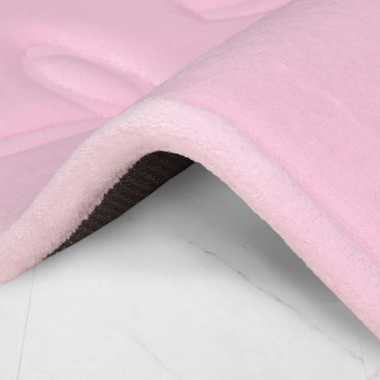 A close-up of the Quilted Memory Foam Bath Mat, 17" x 24", shows its soft, light pink top and dark underside folded on a white marble-patterned surface, highlighting its plush, luxurious texture.