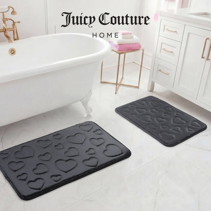 The image shows two black Quilted Memory Foam Bath Mats (2-piece set) adding style to a white bathroom floor by the tub, vanity, and towels. "Juicy Couture Home" appears at the top of the image.