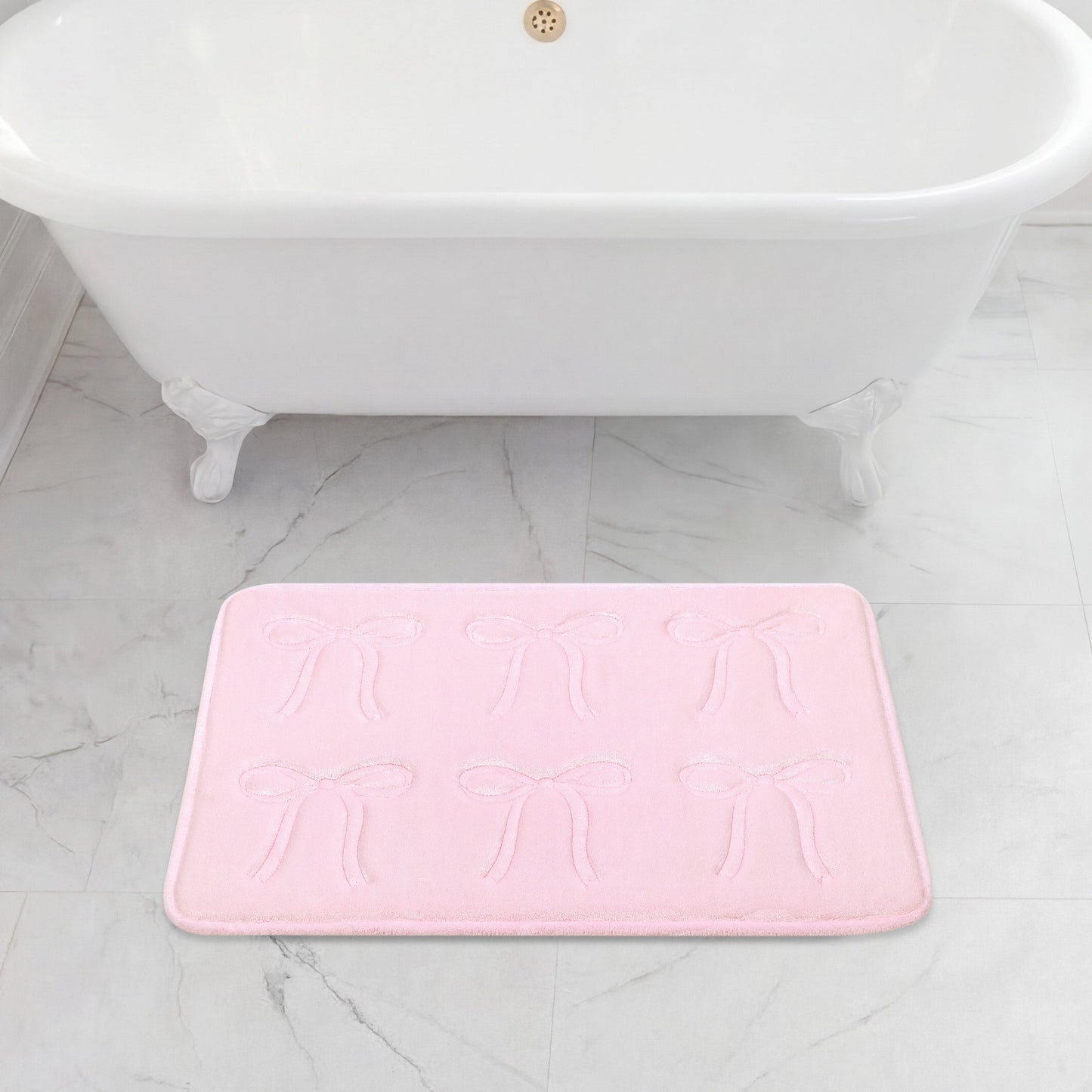A white clawfoot bathtub sits on a gray marble floor, with a 20" x 32" Quilted Memory Foam Bath Mat placed in front, featuring plush comfort and an embossed bow pattern.