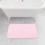 A white clawfoot bathtub sits on a gray marble floor, with a 20" x 32" Quilted Memory Foam Bath Mat placed in front, featuring plush comfort and an embossed bow pattern.