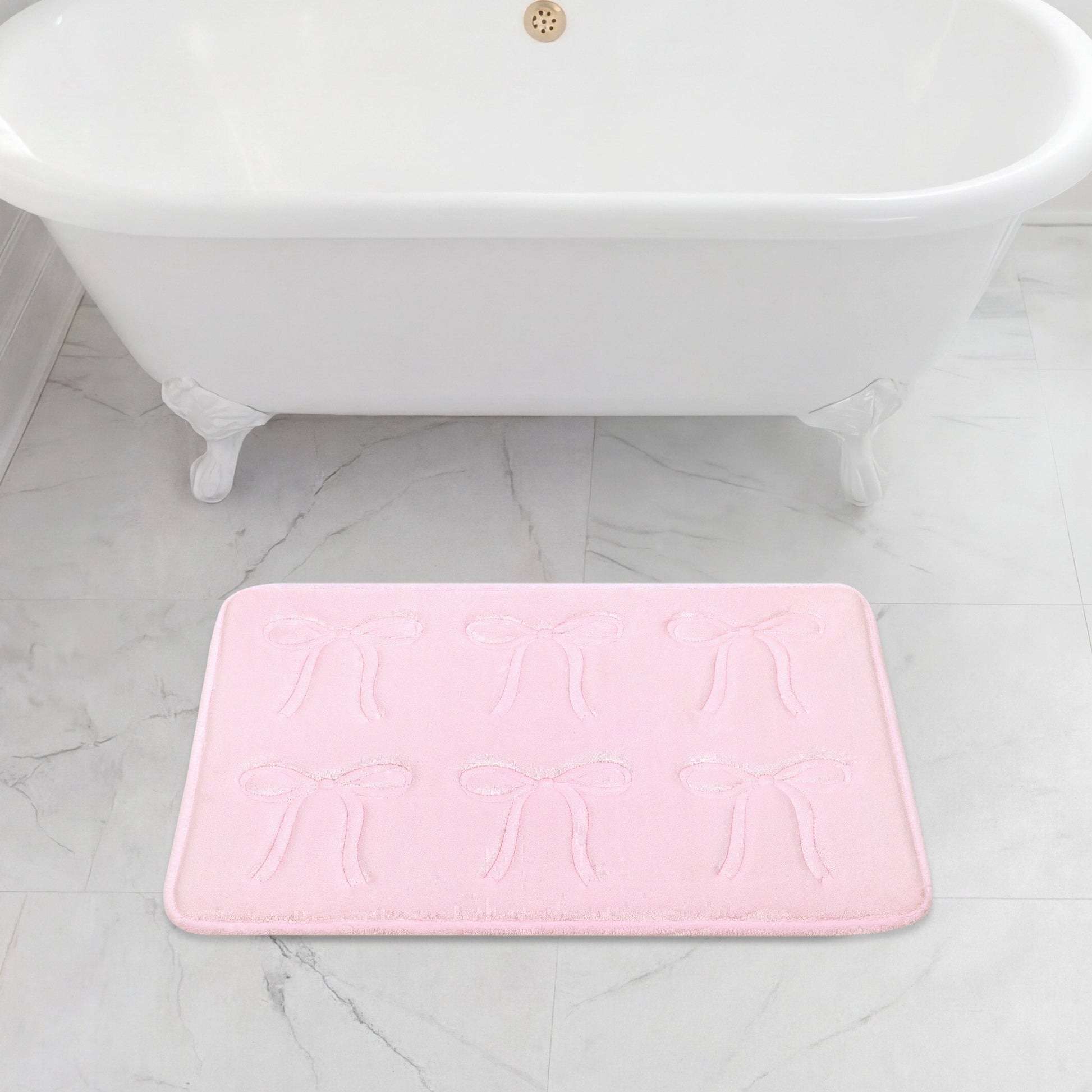 A white clawfoot bathtub sits on a gray marble floor, with a 20" x 32" Quilted Memory Foam Bath Mat placed in front, featuring plush comfort and an embossed bow pattern.
