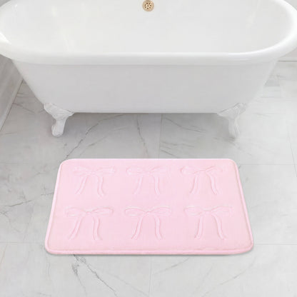 A white clawfoot bathtub sits on a gray marble floor, with a 20" x 32" Quilted Memory Foam Bath Mat placed in front, featuring plush comfort and an embossed bow pattern.
