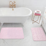 A bright bathroom with a white clawfoot tub, gold faucet, two soft pink Quilted Memory Foam Bath Mats, a gold side table with folded towels, and a white cabinet on marble flooring.