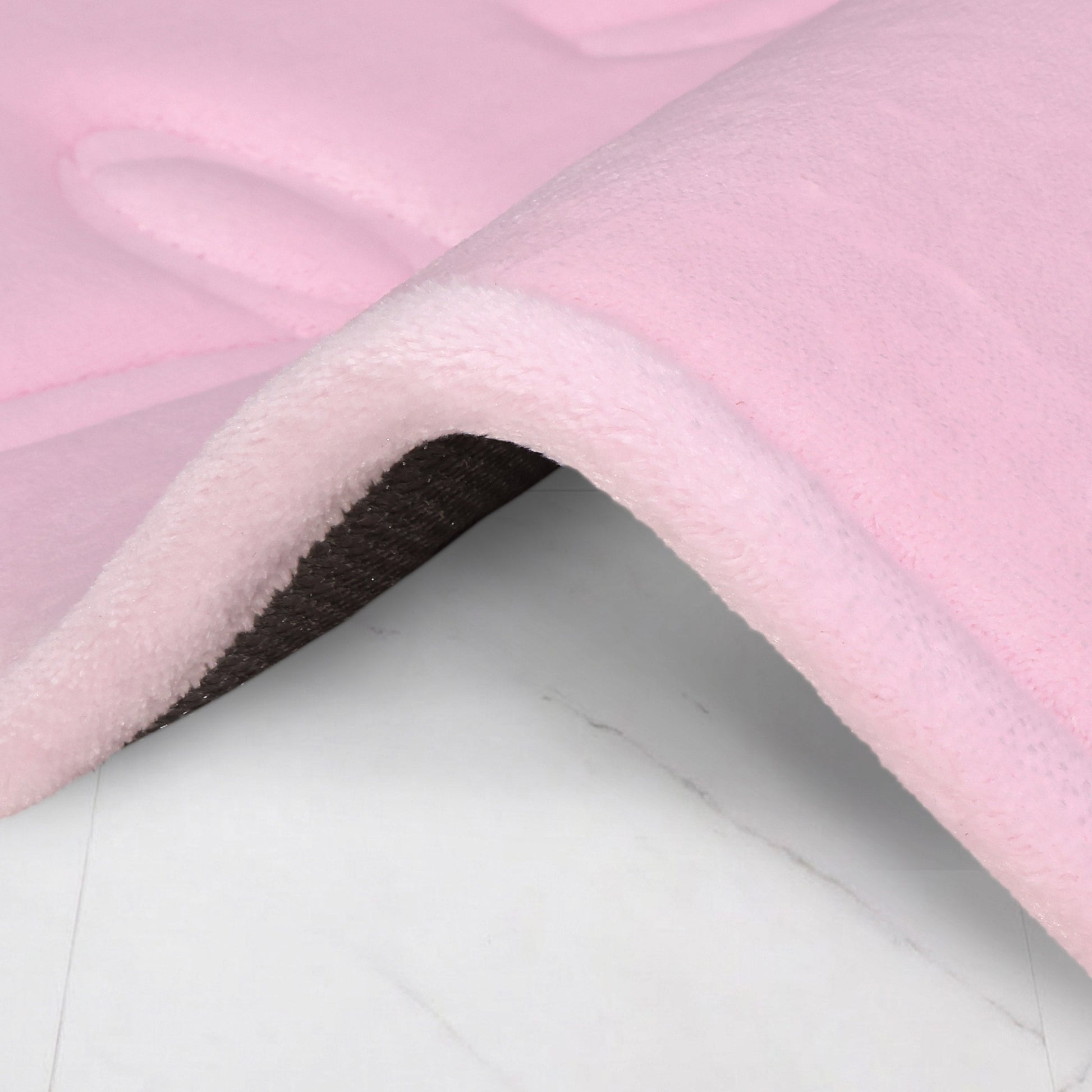 A close-up of the Quilted Memory Foam Bath Mat 2-Piece Set shows its soft, pink, plush quilted surface with a slightly raised edge and darker underside, placed on a smooth, light-colored floor.
