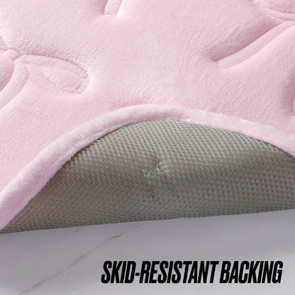 A close-up of the Quilted Memory Foam Bath Mat 2-Piece Set in pink shows its corner flipped, revealing a textured gray skid-resistant backing. The text “SKID-RESISTANT BACKING” appears at the bottom of the image.