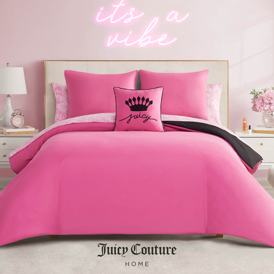 A stylish bedroom features the Juicy Couture Home In The Wild Solid Reversible Bed in a Bag Bedding Set with bright pink bedding and a "Juicy" crown pillow. A pink neon "it’s a vibe" sign glows on the wall behind. Juicy Couture Home logo at bottom.