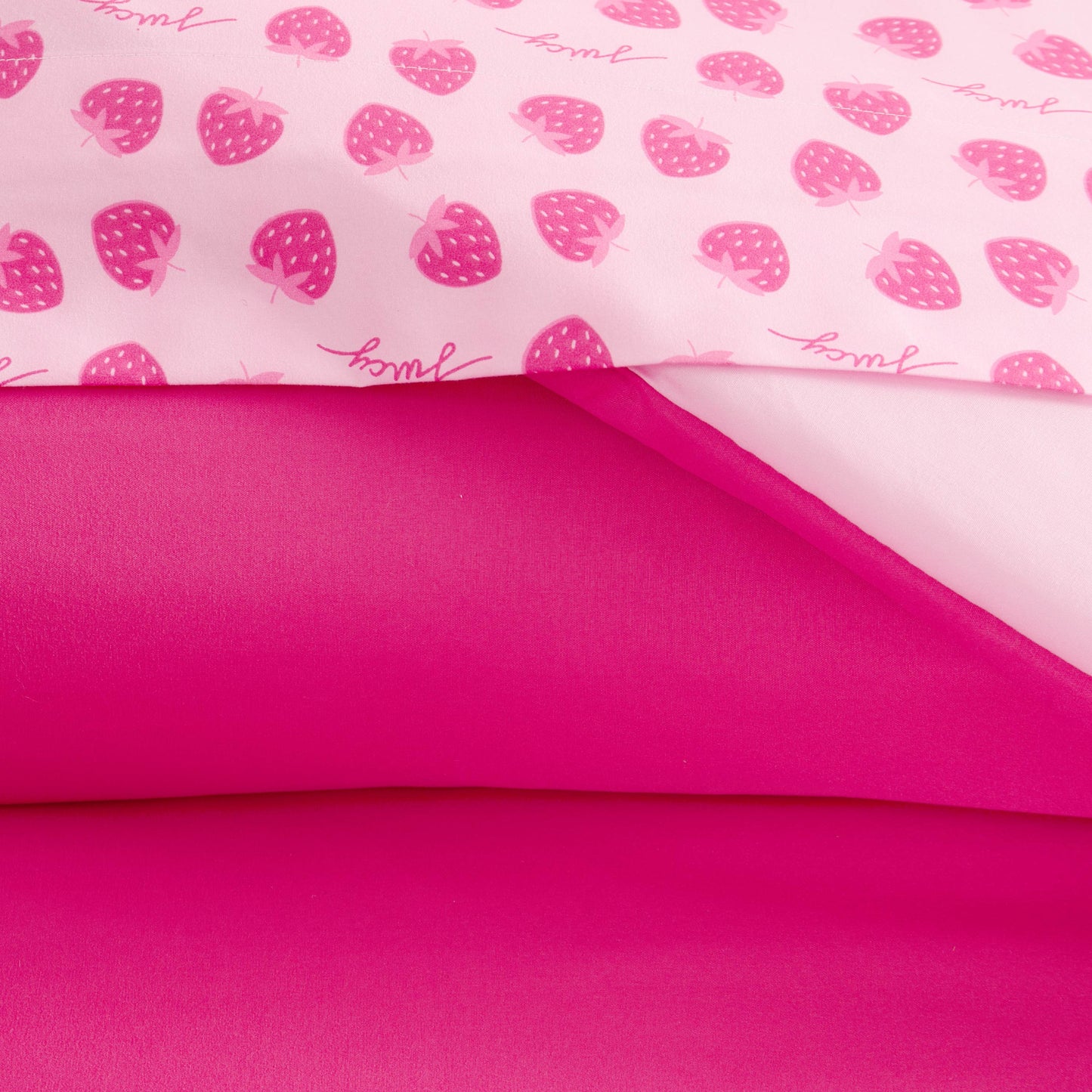 Close-up of the Summer Strawberries Solid Reversible Bed in a Bag Bedding Set, featuring a top sheet with playful strawberry and "yum!" prints on light pink, layered over a solid bright pink sheet for a fun, Juicy Couture-inspired look.