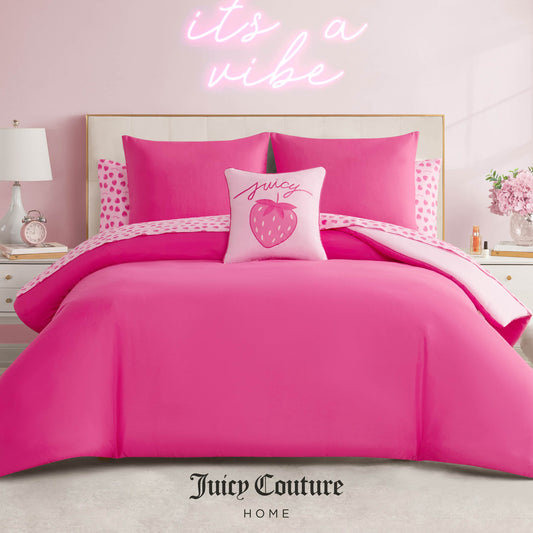 A stylish bedroom features a bright pink Juicy Couture bed with the Summer Strawberries Solid Reversible Bed in a Bag Bedding Set and a strawberry-themed pillow. Above the bed, the light pink wall has a neon "its a vibe" sign. White nightstands and lamps flank the bed.