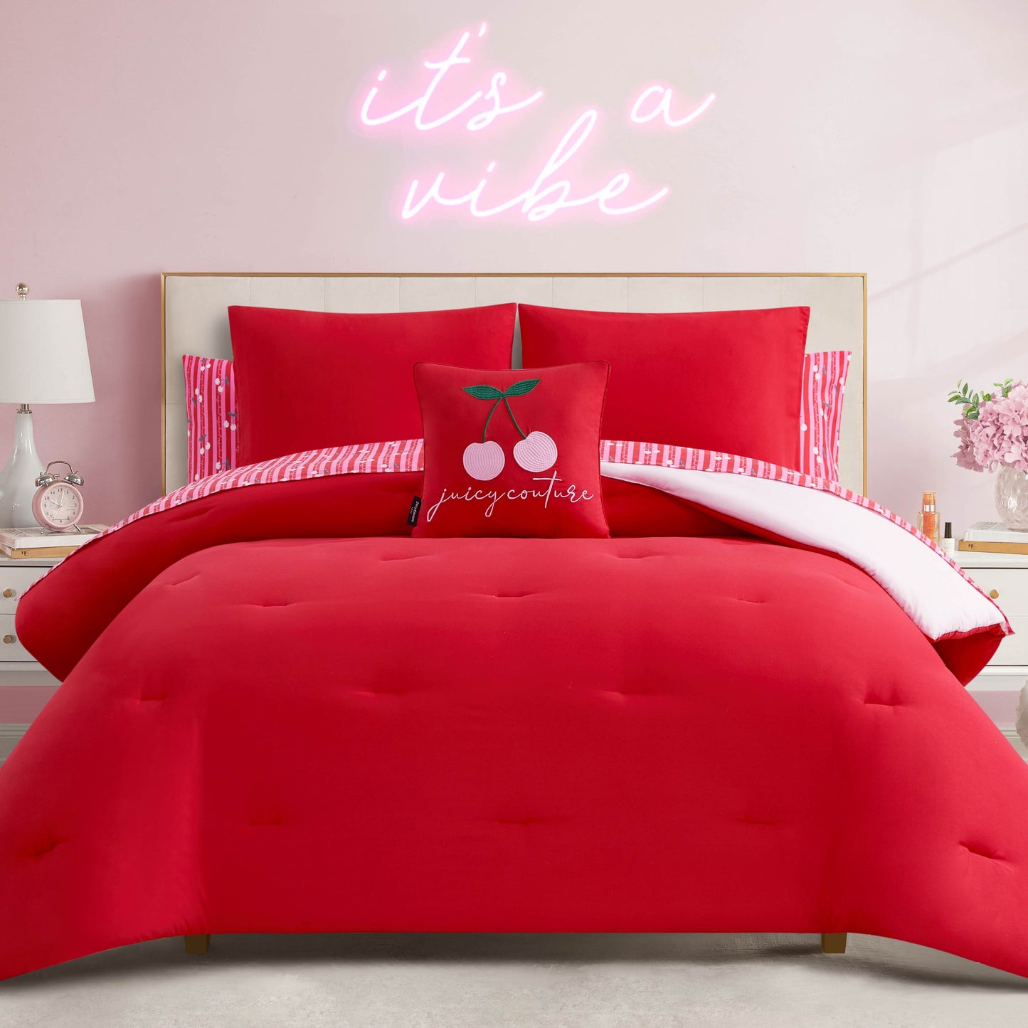 A modern bedroom features the Cherry Script Solid Reversible Bed in a Bag Bedding Set, cherry-themed and striped accent pillows, and a gold bed frame. Above the bed, a neon "it's a vibe" sign glows, creating a stylish atmosphere.