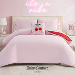 A neatly made bed with the Cherry Script Solid Reversible Bed in a Bag Bedding Set, cherry-themed accents, red-accented sheets, a modern white nightstand and lamp, plus a pink neon “it’s a vibe” sign above the bed.