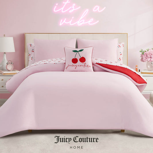 A neatly made bed with the Cherry Script Solid Reversible Bed in a Bag Bedding Set, cherry-themed accents, red-accented sheets, a modern white nightstand and lamp, plus a pink neon “it’s a vibe” sign above the bed.
