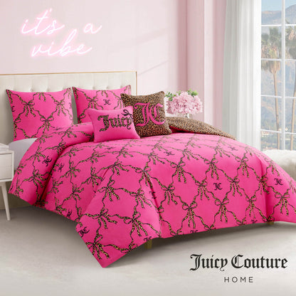 The Cheetah Bow Trellis Reversible Comforter Set in pink with leopard and gold accents adds chic flair to a bright room. A neon "it's a vibe" sign glows on the wall, while palm trees and mountains can be seen through the window.