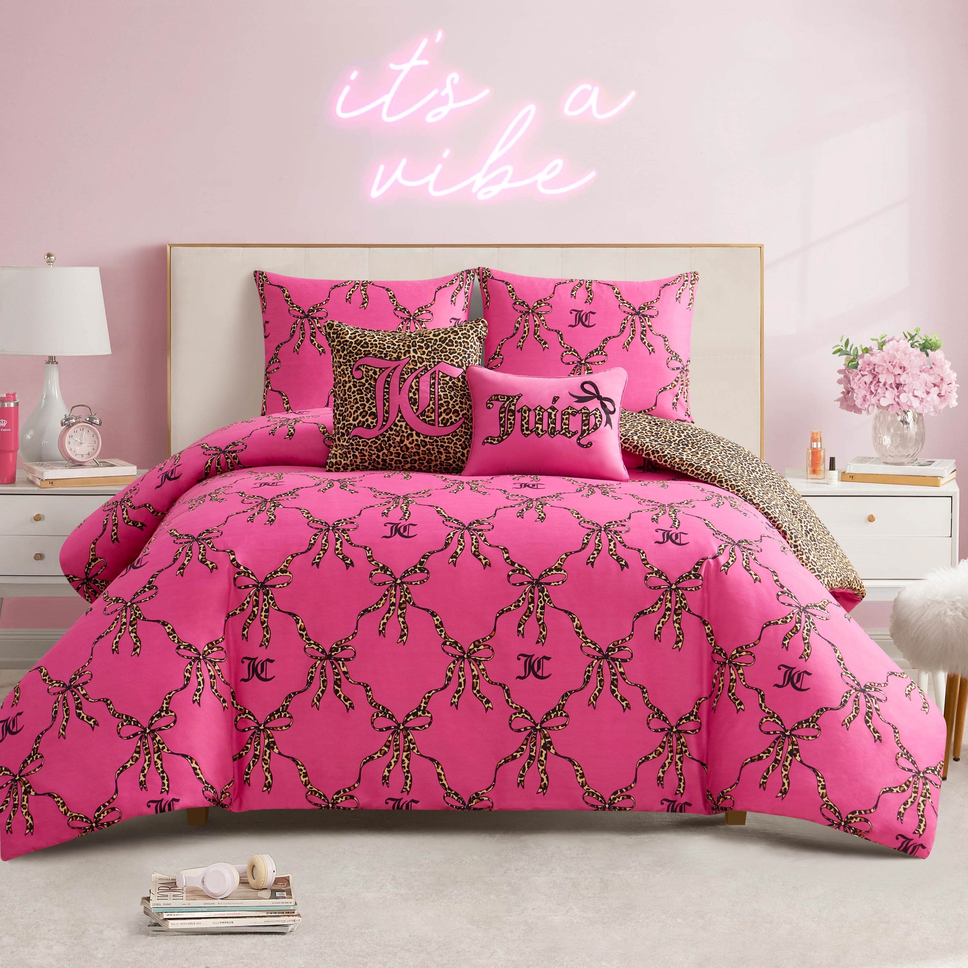 A stylish bedroom with a pink Cheetah Bow Trellis Reversible Comforter Set, matching pillows, white bed frame, pink walls, and a neon “it’s a vibe” sign—ideal for fans of reversible bedding and fashion-inspired decor.