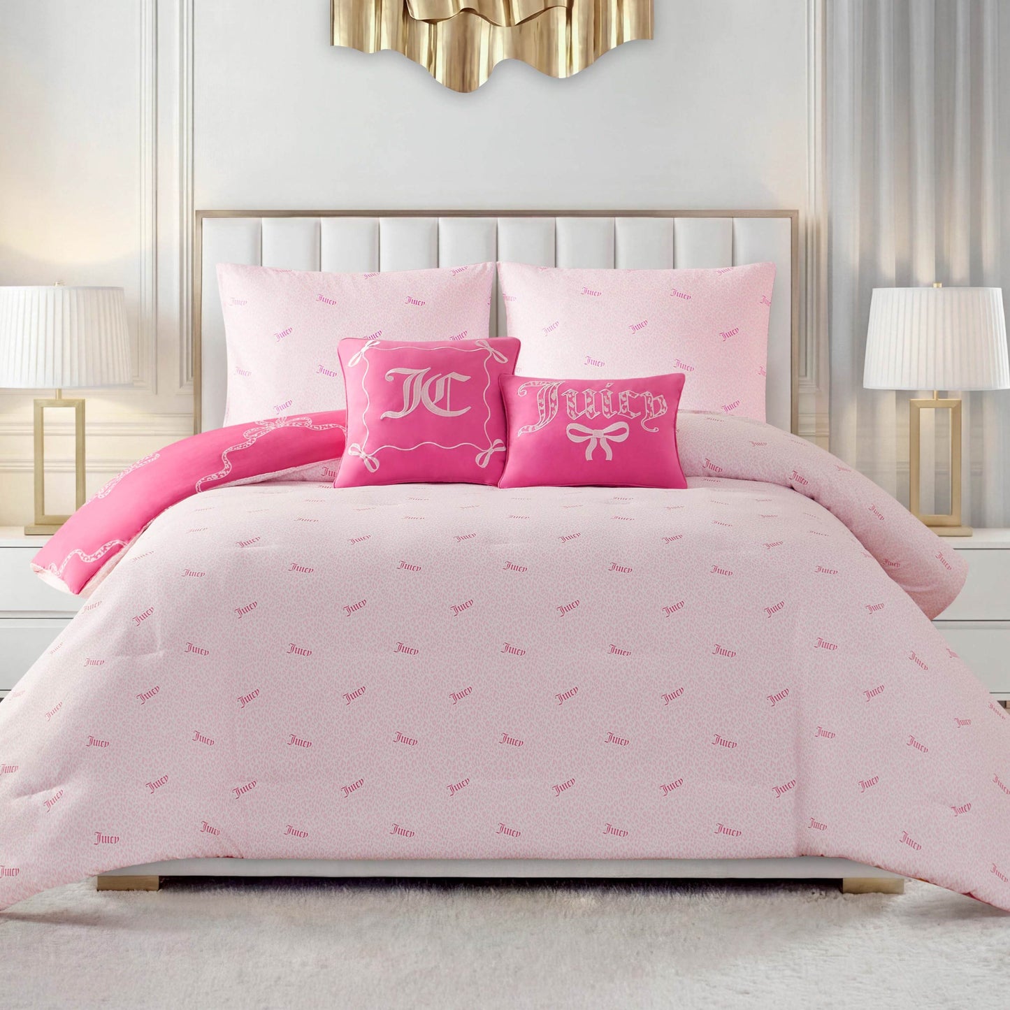 A neatly made bed features the Chevron Leopard Bow Reversible Comforter Set in light pink with embroidered pillows—one with white initials, the other says “Juicy” with a bow. Two white nightstands and lamps sit on each side of the bed.