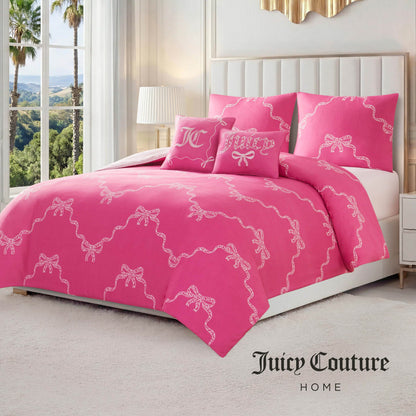 A neatly made bed with a bright pink Chevron Leopard Bow Reversible Comforter Set featuring white bow patterns, matching embroidered pillows, and a white tufted headboard in a sunlit bedroom with large windows and palm trees outside.