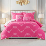 A modern bedroom with white walls features a neatly made bed dressed in the Chevron Leopard Bow Reversible Comforter Set, decorated with white bows and matching pillows, positioned between two white nightstands and lamps and accented by a gold wall decoration.