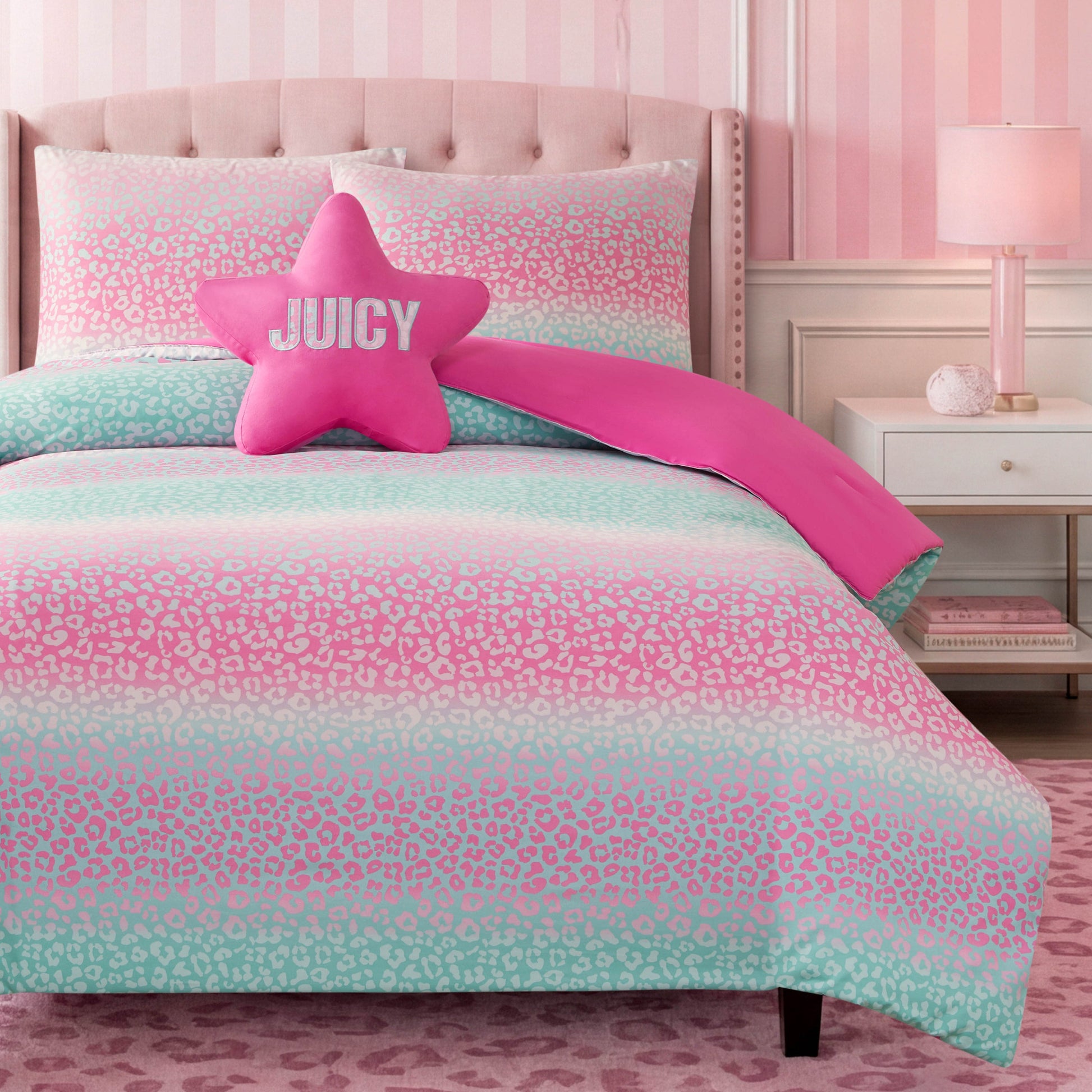 A vibrant kids’ bedroom highlights the Kids Rainbow Ombre Leopard Reversible Comforter Set, which features playful pink and mint leopard-print bedding. The room is accented with a pink star-shaped JUICY pillow, striped pink wallpaper, a coordinating pink lamp, and a subtle animal print pattern rug—perfectly capturing the fun and stylish Juicy Couture aesthetic.