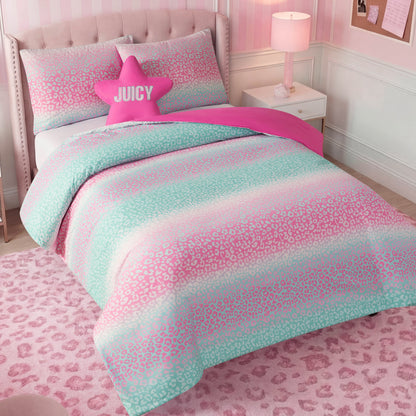 A pastel-themed kids bedroom set featuring the Kids Rainbow Ombre Leopard Reversible Comforter Set, coordinated pillows, a pink JUICY star pillow, a pink table lamp, and a soft pink leopard print rug.