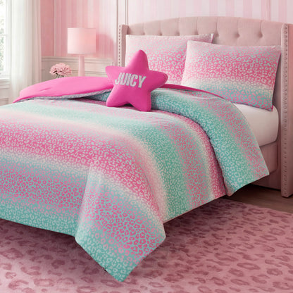 A stylish kids bedroom set features the Kids Rainbow Ombre Leopard Reversible Comforter Set from Juicy Couture, with its pink and mint green leopard print comforter, accented by a star-shaped JUICY pillow and a soft pink rug, all set against vibrant pink walls and coordinating furniture.
