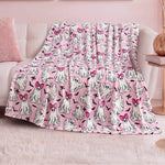 The Halloween Plush Throw Blanket 50" x 60", featuring cute white ghosts—some with pink bows—is draped over a white sofa in a pastel-themed room with pink decor and a fluffy rug, making it perfect for chic Halloween home decor.