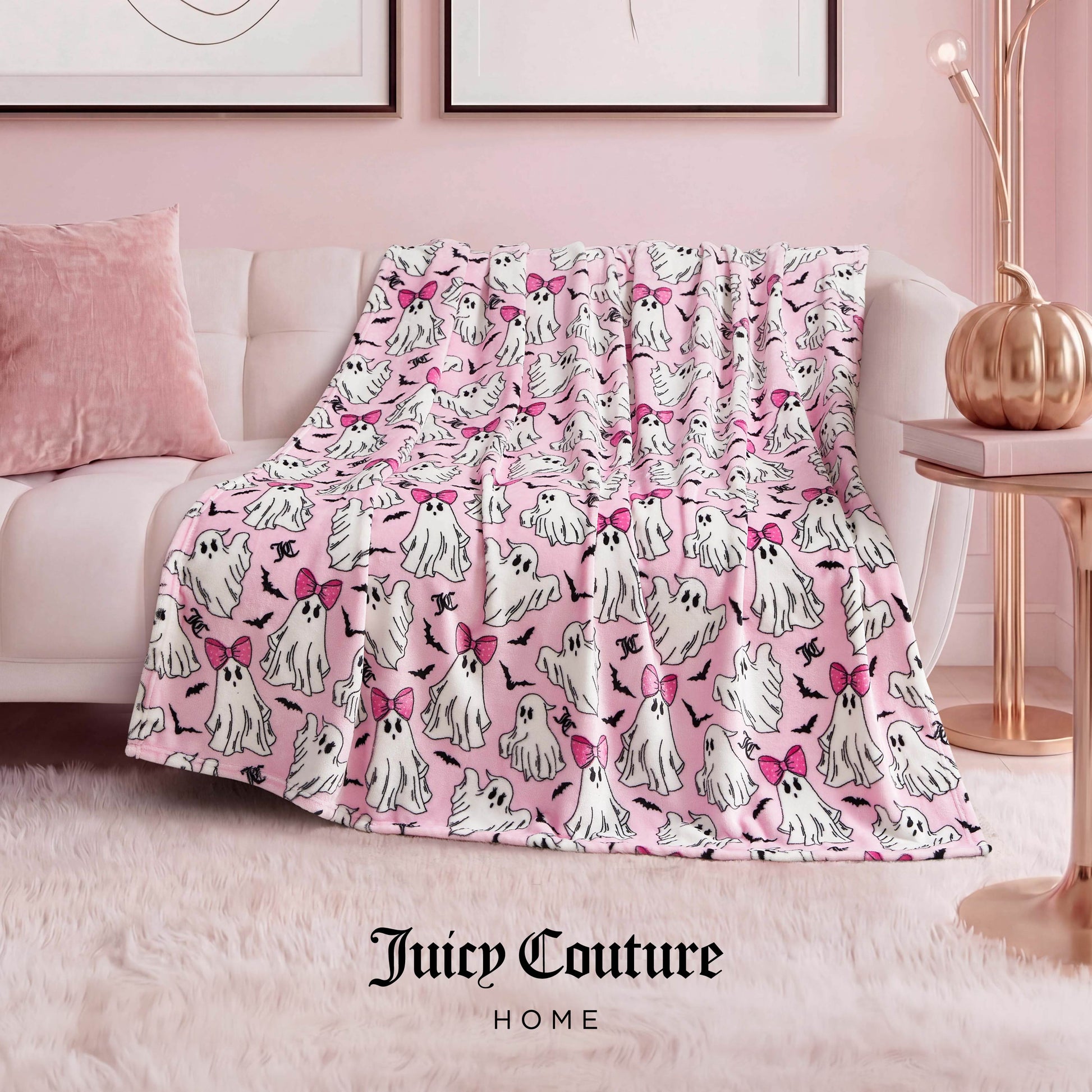 The Halloween Plush Throw Blanket 50" x 60", featuring white cartoon ghost dogs with pink bows, is draped over a sofa in a chic pink-themed living room—an adorable Juicy Couture Home accent for Halloween decor.